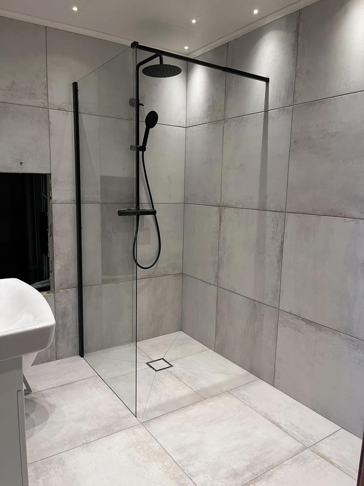 Microcement Halmstad – Walk-in dusch med svart blandare och storformatiga plattor