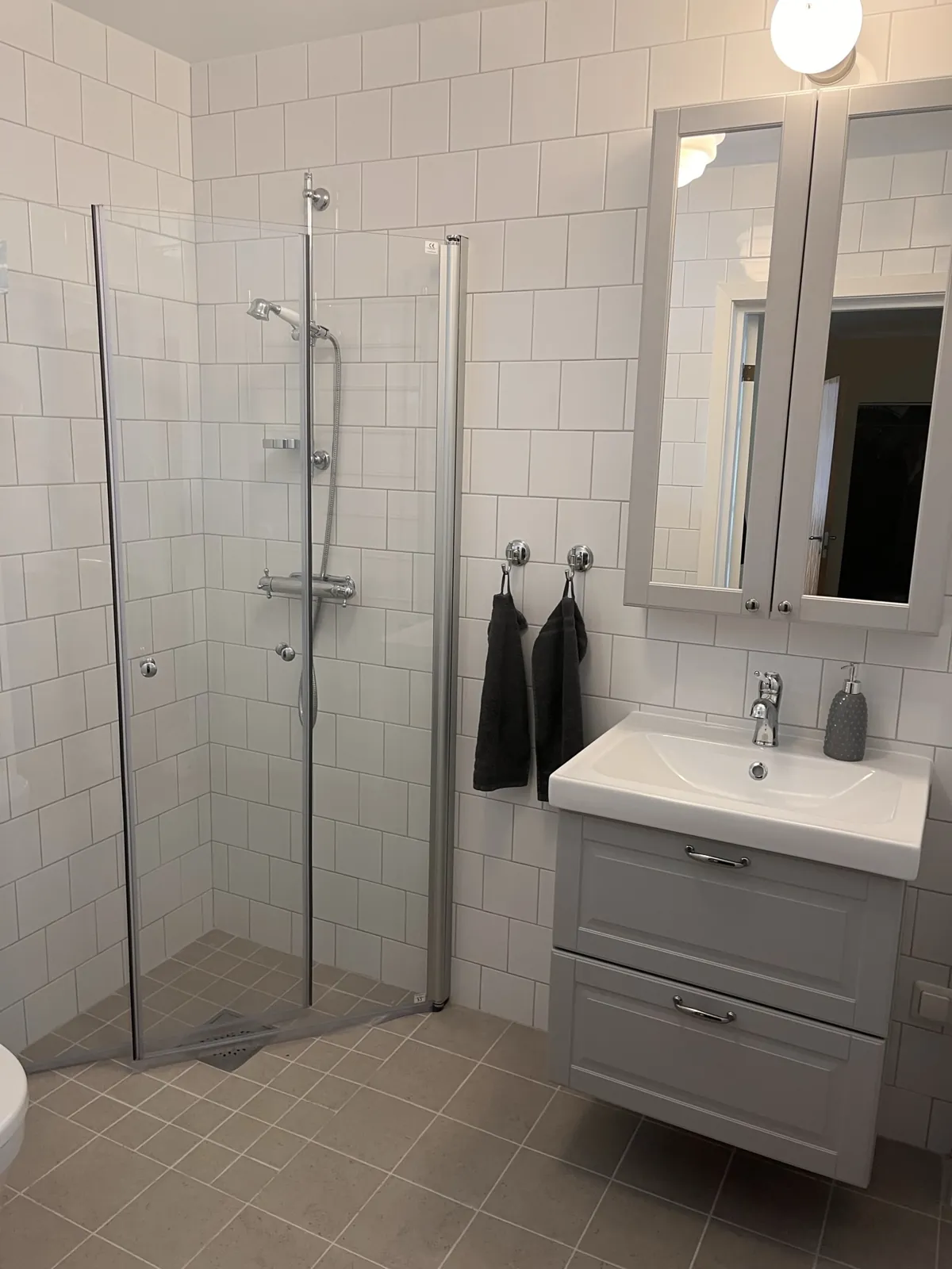 Badrumsrenovering Harplinge – Badrum med vitt kakel, grå kommod och duschhörna i glas